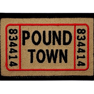 Può includere: Una toppa ricamata di colore beige e nero con cuciture rosse. La toppa ha la forma di un biglietto e dice "POUND TOWN" con i numeri "834414" su entrambi i lati.