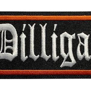 Peut inclure: Écusson brodé avec le mot "Dilligaf" en lettres gothiques blanches sur fond noir. L'écusson a une bordure orange et est de forme rectangulaire. Idéal pour les vestes, sacs ou autres vêtements.