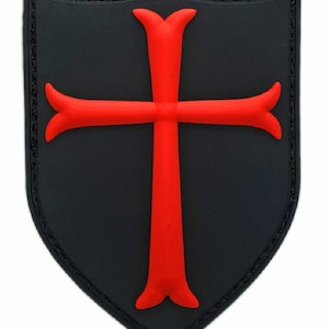 May include: A black and red embroidered patch in the shape of a shield with a red cross inside.