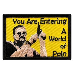 May include: A yellow embroidered patch with a black border. The patch features a cartoon image of a man holding a gun and the text "You Are Entering A World of Pain".