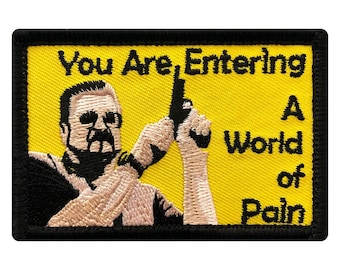 May include: A yellow embroidered patch with a black border. The patch features a cartoon image of a man holding a gun and the text "You Are Entering A World of Pain".