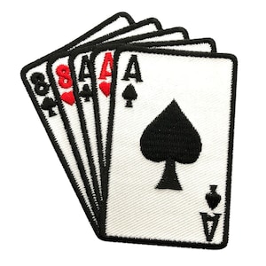 May include: A white patch with black stitching showing a set of five playing cards, including the 8, 4, Ace, Ace, and Ace of spades. The cards are arranged in a fan shape with the Ace of spades on top.