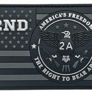 Op de afbeelding: Een zwart-witte patch met een Amerikaans vlagontwerp. De patch heeft een cirkel met de tekst "America's Freedom The Right To Bear Arms" en een Amerikaanse zeearend met de tekst "2A" in een cirkel. De tekst "2ND" staat in de linkerbovenhoek van de patch.