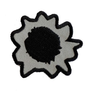 May include: A gray and black embroidered patch depicting a bullet hole. The patch has a black center with a gray ring around it, and a black outline.