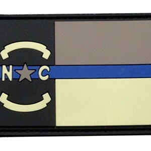 May include: A black and white patch with a blue stripe. The patch features a star and the letters "N.C." in a circle.