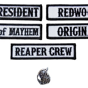 Puede incluir: Cinco parches rectangulares blancos con texto bordado en negro: "V. PRESIDENT", "REDWOOD", "MEN of MAYHEM", "ORIGINAL" y "REAPER CREW". También se incluye un pin de segador plateado.