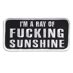 Pode incluir: Etiqueta bordada preta com costuras brancas. A etiqueta diz "I'm a ray of fucking sunshine."
