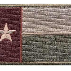 Peut inclure: Un patch brodé représentant le drapeau du Texas. Le patch est de couleur marron, blanc et vert et présente une étoile blanche sur un fond marron, une bande blanche et une bande verte.