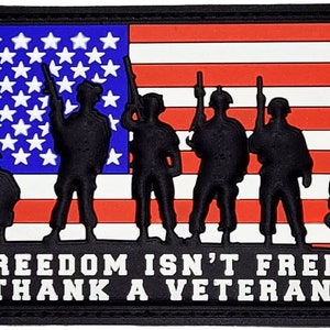 Op de afbeelding: Een zwart-witte patch met een silhouet van vijf soldaten die voor een Amerikaanse vlag staan. De tekst "FREEDOM ISN'T FREE! THANK A VETERAN" staat onder de soldaten.