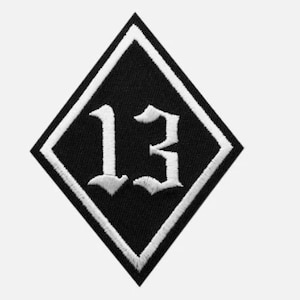 May include: A black diamond-shaped patch with a white embroidered number "13" in a gothic font.