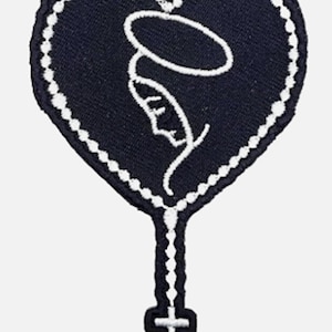 May include: A navy blue heart-shaped patch with a white beaded border. The patch features a white outline of a religious figure with a halo, and a rosary leading to a cross. The design is embroidered.