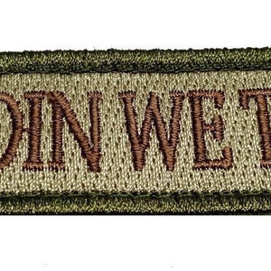 May include: A green and tan embroidered patch with the text "IN ODIN WE TRUST" in brown thread.