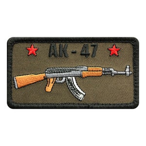 May include: A green embroidered patch with a black border featuring a stylized image of an AK-47 rifle with the text "AK-47" and two red stars.