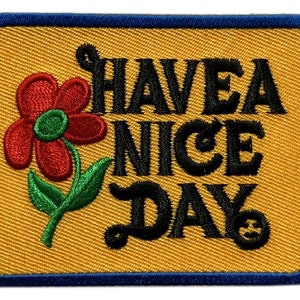 May include: A yellow embroidered patch with a blue border. The patch features a red flower with a green stem and the text "HAVE A NICE DAY".