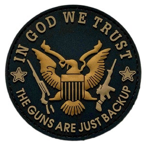 Peut inclure: Un patch rond noir et or avec les mots "In God We Trust" et "The Guns Are Just Backup" entourant un aigle doré avec un bouclier et deux armes à feu.