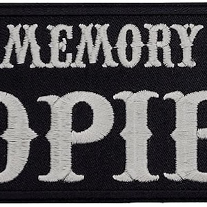 Peut inclure: Écusson brodé noir avec du texte blanc qui dit "In Memory of 'Opie'".