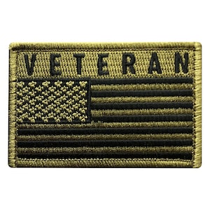 May include: A green and black embroidered patch with the word "Veteran" above an American flag.