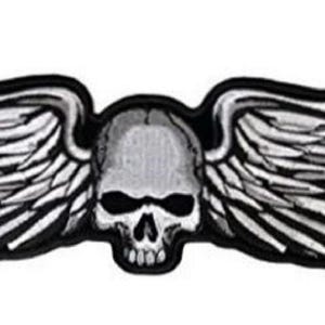 May include: A black and white embroidered patch of a skull with wings. The skull has a detailed design with a prominent nose and eye sockets. The wings are spread out and have a feathered design.