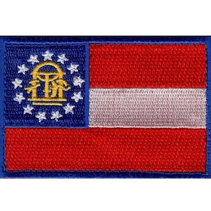 May include: An embroidered patch of the Georgia state flag. The flag is blue with a gold state seal in the upper left corner and a white and red stripe across the bottom. The seal features a gold arch with three gold figures standing beneath it.