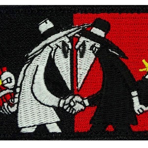 May include: Embroidered patch featuring two figures shaking hands, one in white and one in black, against a red and black background. Each figure holds a lit stick of dynamite.