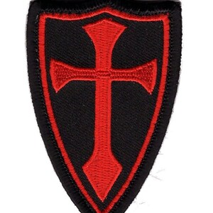 May include: A black embroidered patch with a red cross inside a shield shape.