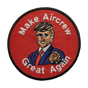 Peut inclure: Un écusson brodé circulaire rouge et noir avec un contour blanc. L'écusson présente une image de dessin animé d'un homme aux cheveux blonds portant un costume bleu et une cravate rouge. Le texte "Make Aircrew Great Again" est écrit en blanc autour de l'image.