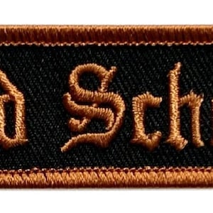 May include: A brown embroidered patch with the words "Old School" in a black gothic font on a black background.