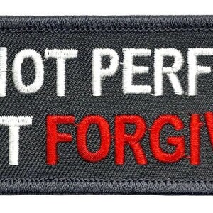Puede incluir: Parche bordado gris con texto blanco que dice "No soy perfecto, solo perdonado" con la palabra "perdonado" en rojo.