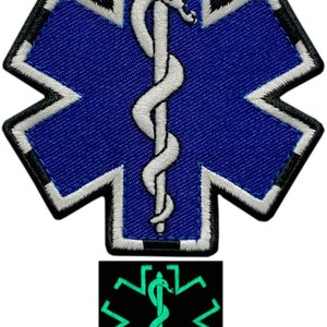Könnte beinhalten: Ein blauer und weißer gestickter medizinischer Lebensstern-Patch mit einer weißen Schlange und einem Stab. Der Patch hat einen schwarzen Rand und wird auf einem schwarzen Hintergrund mit einer grün leuchtenden Version des Patches gezeigt.