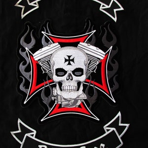 May include: Black and white embroidered patch with a skull and crossbones design. The skull has a black cross on its forehead. The crossbones are formed by two engine pistons. The patch has a red and white cross in the center and flames on the sides. The patch has two banners at the top and bottom. The top banner says "Live Free" and the bottom banner says "Ride Free".