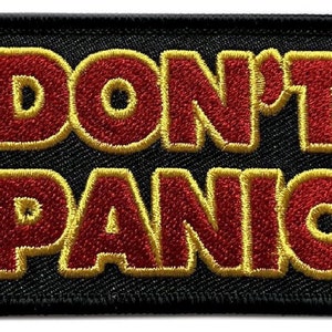 Könnte beinhalten: Schwarzer gestickter Aufnäher mit gelber Umrandung. Der Aufnäher sagt "DON'T PANIC" in roten Buchstaben.
