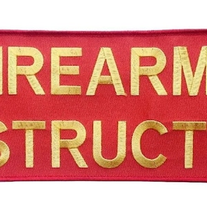 Könnte beinhalten: Roter Stoff-Patch mit goldfarbener Stickerei, auf dem "FIREARMS INSTRUCTOR" steht.