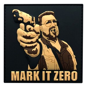 May include: A black and tan embroidered patch with a cartoon image of a man holding a gun and the text "MARK IT ZERO".
