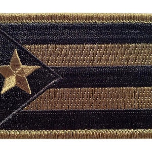 May include: A brown and black embroidered patch with a star and stripes design. The patch is surrounded by a brown border.