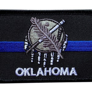 May include: Black embroidered patch with a blue line, a white outline of the Oklahoma state seal, and the word "OKLAHOMA" in white.