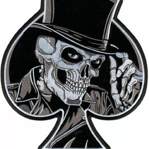 May include: Black and white embroidered patch of a skull wearing a top hat and a leather jacket. The skull is in the shape of a spade playing card.