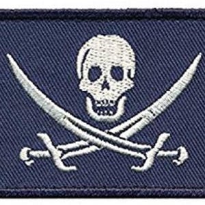 Pode incluir: Patch azul escuro com uma caveira e ossos cruzados bordados em branco.