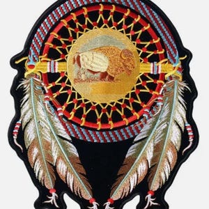 Op de afbeelding: Geborduurde patch met een dromenvanger ontwerp. De patch heeft een zwarte achtergrond met een centrale gouden cirkel met een bison afbeelding. Rode, blauwe en gouden accenten omringen de cirkel, met twee gedetailleerde veren.