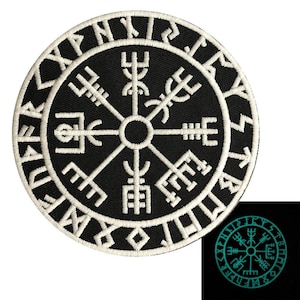May include: A black and white embroidered patch with a compass design and runes around the edge. The compass has four points with symbols at each point. The patch glows green in the dark.