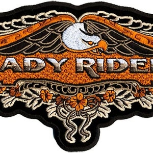 Peut inclure: Un patch brodé avec un motif d'aigle orange et noir. Le patch présente le texte "LADY RIDER" en police argentée.