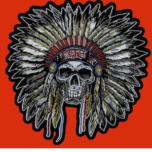 May include: A black and white embroidered patch of a skull wearing a Native American headdress with red, white, and blue feathers. The headdress has a beaded band with a red, white, and blue pattern.