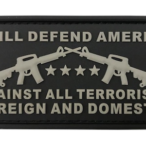 May include: Black rectangular patch with the text "I WILL DEFEND AMERICA AGAINST ALL TERRORISTS FOREIGN AND DOMESTIC." Two crossed rifles and five stars are featured in silver. The patch is a military or patriotic item.