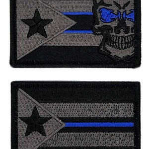 May include: Two black embroidered patches with a gray Puerto Rican flag design. The top patch features a gray skull with blue eyes. The bottom patch has a thin blue line across the flag.