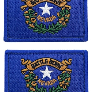 May include: Two blue embroidered patches featuring the state flag of Nevada. The patches feature a white star, a gold ribbon with the words "Battle Born" and a green wreath with the word "Nevada".