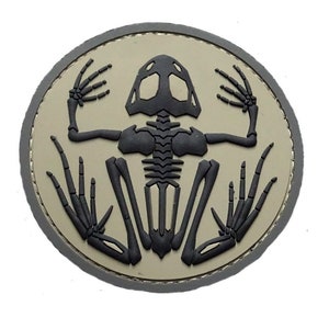 May include: A round, tan-colored patch with a black, detailed skeleton of a frog in the center.