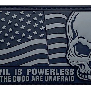 May include: A black and white embroidered patch with an American flag and a skull. The text "EVIL IS POWERLESS IF THE GOOD ARE UNAFRAID" is written below the flag and skull.