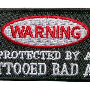 May include: Black embroidered patch with white text that reads "WARNING PROTECTED BY A TATTOOED BAD ASS" and a red oval with white text that reads "WARNING".