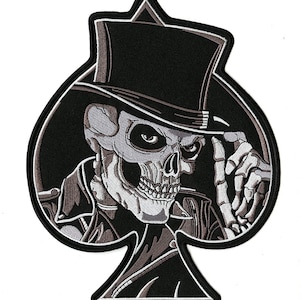 May include: Black and white embroidered patch of a skull wearing a top hat and a leather jacket, in the shape of a spade playing card.