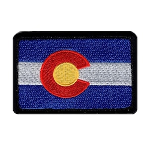 May include: Embroidered patch depicting the Colorado state flag. The design features a blue background with a white stripe, a red 'C' shape, and a gold disc. The patch is framed by a black border.