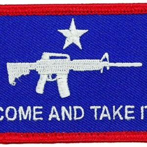 Puede incluir: Un parche bordado azul y rojo con una silueta blanca de un rifle y una estrella. El texto "COME AND TAKE IT" está bordado en blanco debajo del rifle.